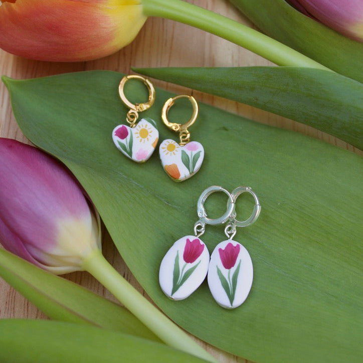 Pair of floral earrings on a green leaf with tulips in the background